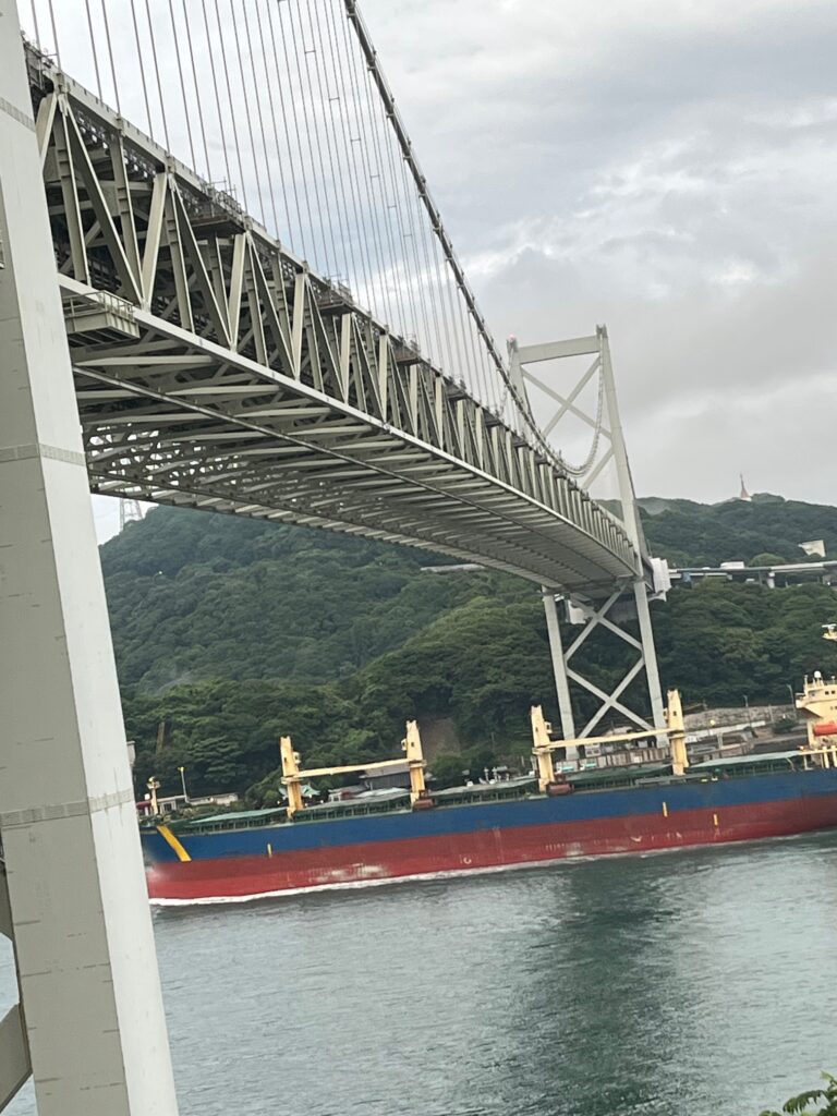 関門海峡に架かる関門橋、大型タンカーが橋の下をくぐっていて、向かいには九州が見えます。