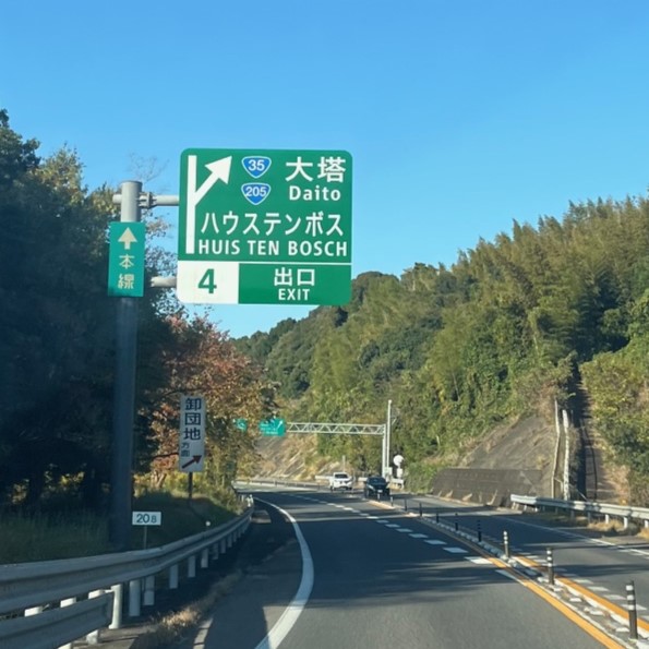 山に挟まれた、長崎自動車道、佐世保大塔インターとハウステンボスと書かれた標識が見える