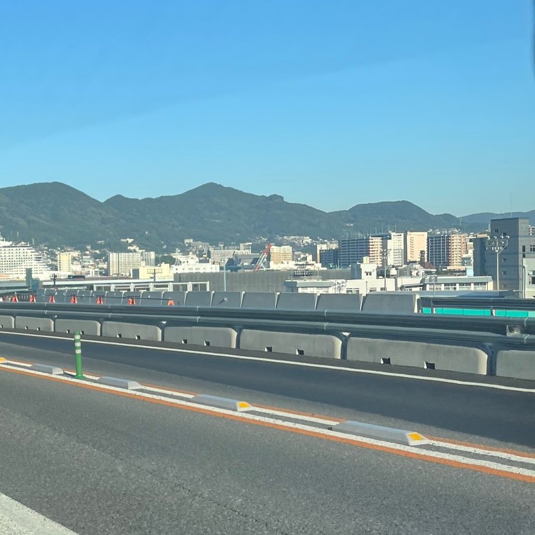 佐世保道路から望む佐世保の街並み、青い空と山のふもとにビルやマンションが並んでいる