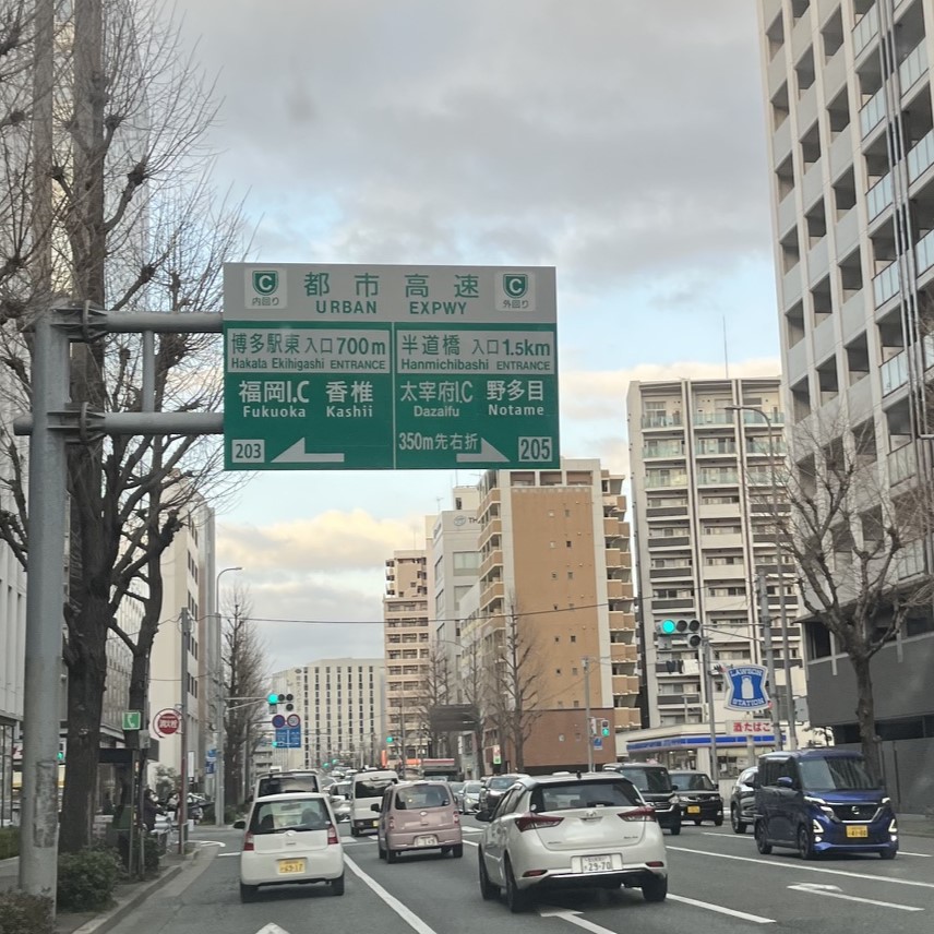 ビル群に囲まれた道には福岡都市高速の大きな案内看板がある