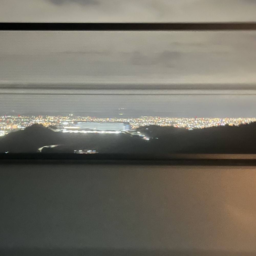 夜も更けた新名神高速道路の高台から見える大阪の夜景、彩鮮やかな光の水平線が広大に広がっている
